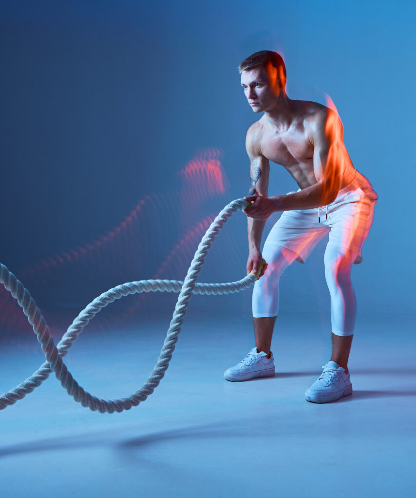 Isolated figure of half naked bodybuilder with the rope in studio on blue background.