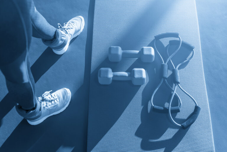 Woman feet near mat with expander and dumbbells